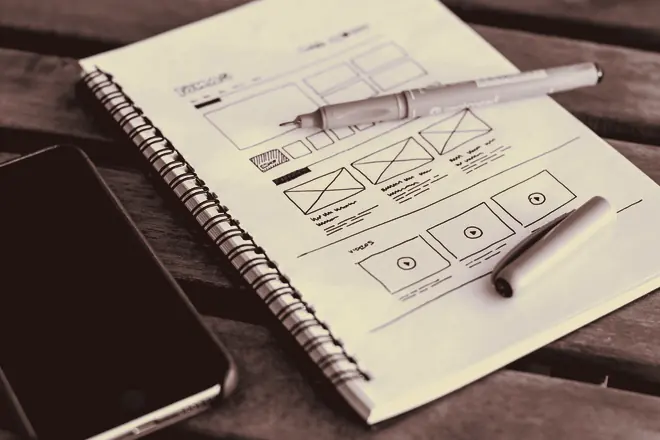 Wireframe layout sketches drawn on a notepad beside a pen.